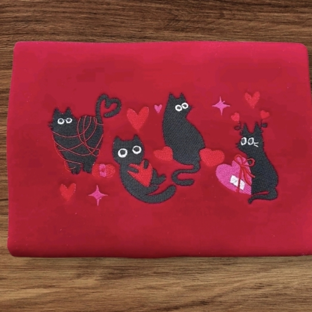 A Red sweatshirt with a black cat design. The cats are holding hearts and yarn i